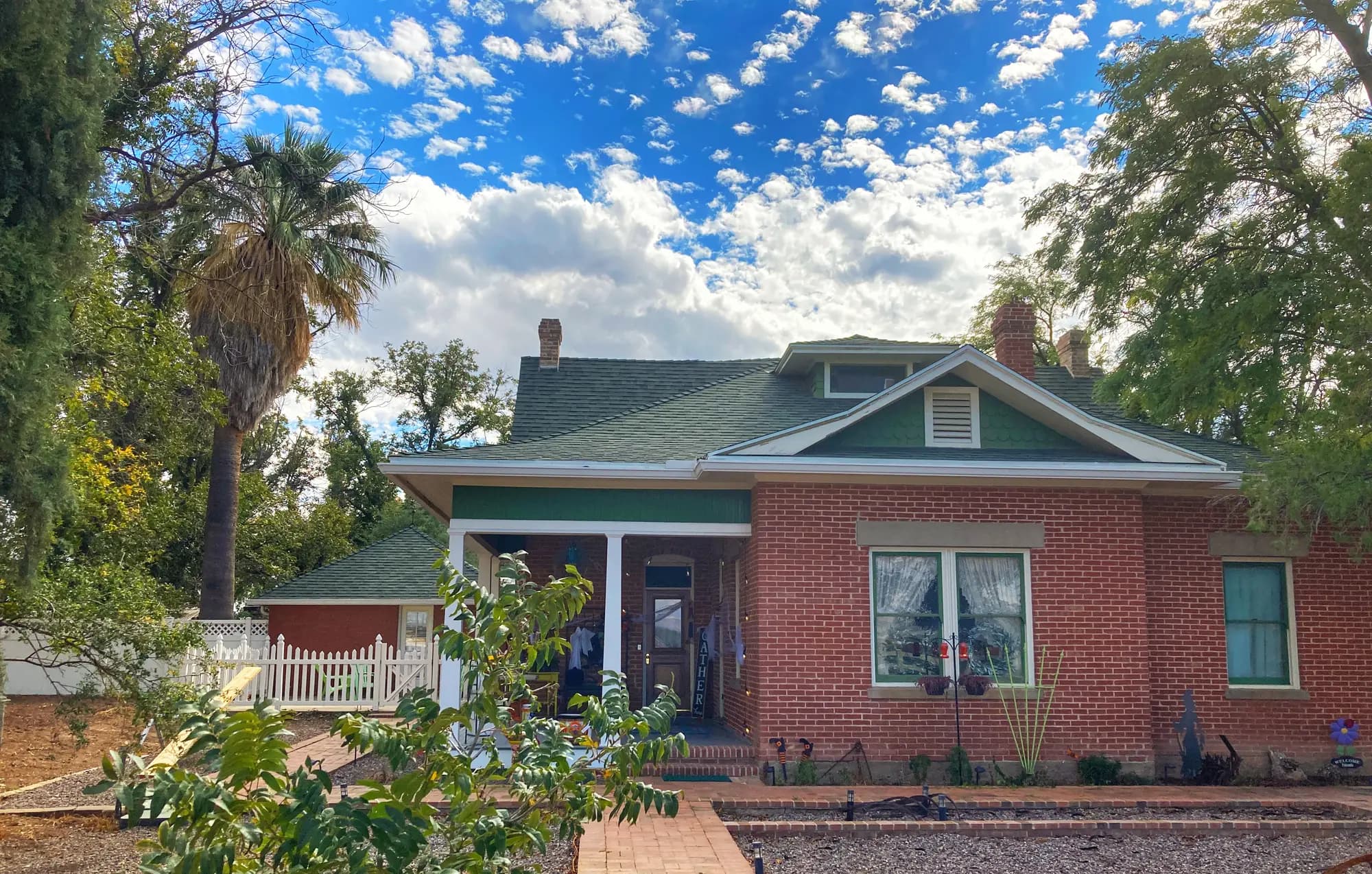 The front of the historic brick farmhouse, with a green roof and mature trees